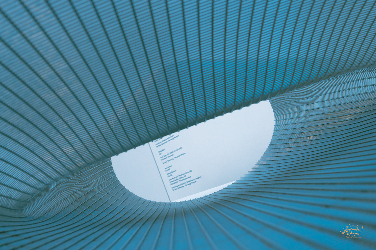 Woven metal mesh sculpture in cyan tones toward an oval skylight