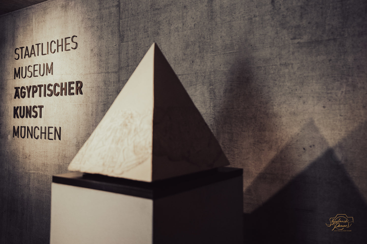 Alabaster pyramid before a concrete wall with the museum name in German