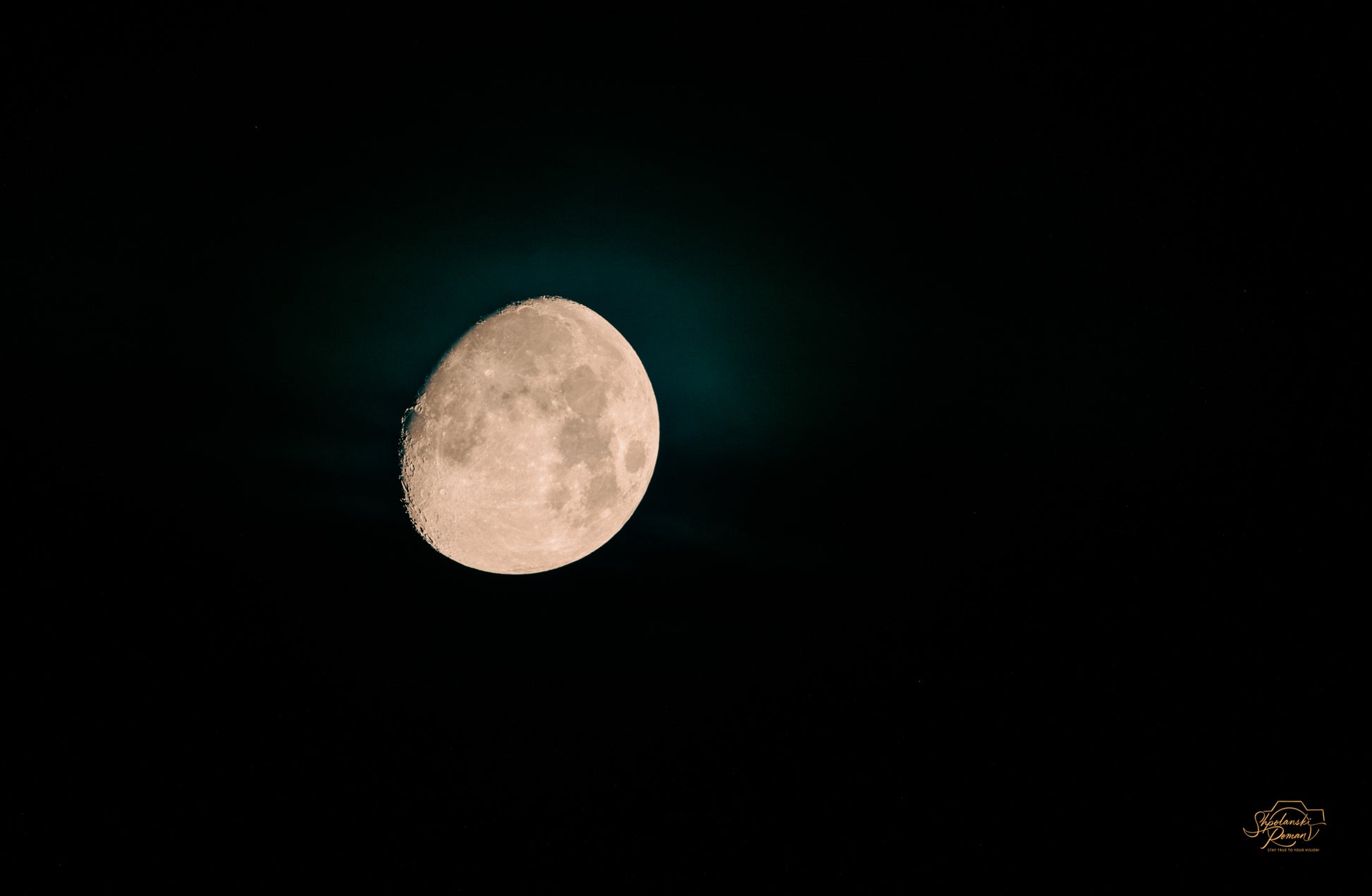 The moon surrounded by a teal-green glow in a dark sky