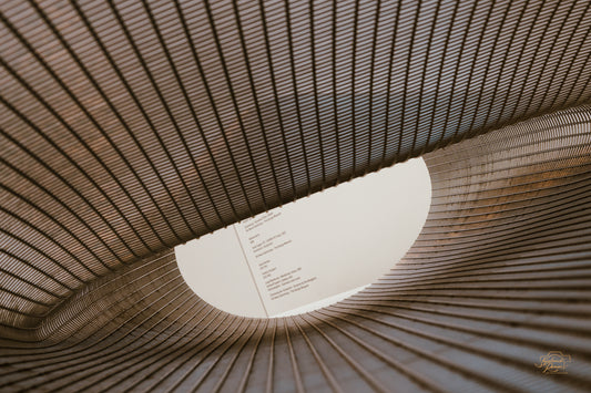 Woven metal mesh sculpture sweeping toward an oval skylight, amber tones