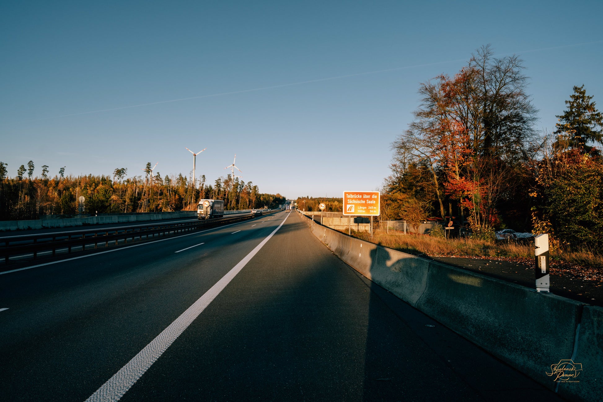 An open road lined with autumn trees at sunset