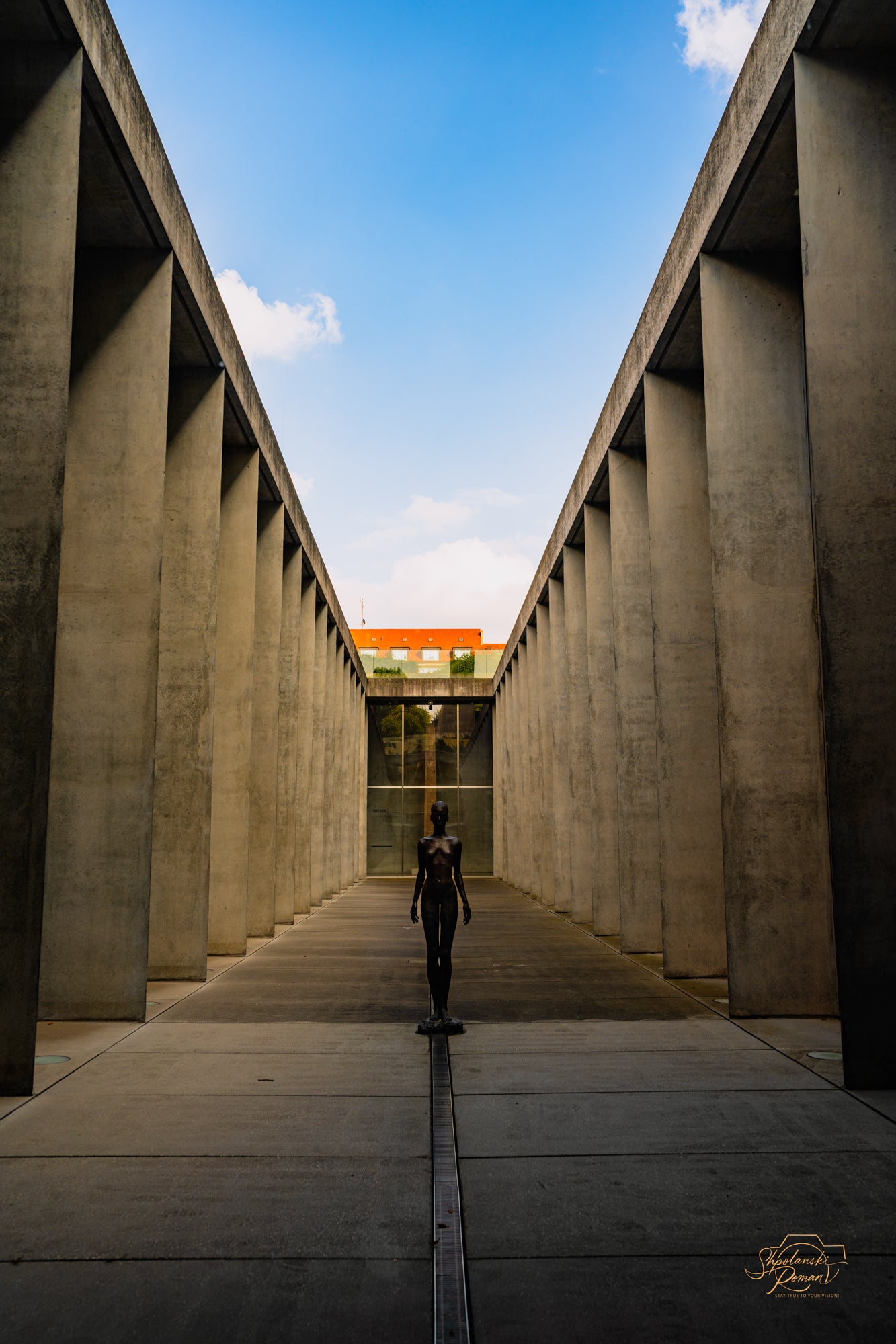A lone figure in a symmetrical concrete corridor under blue sky