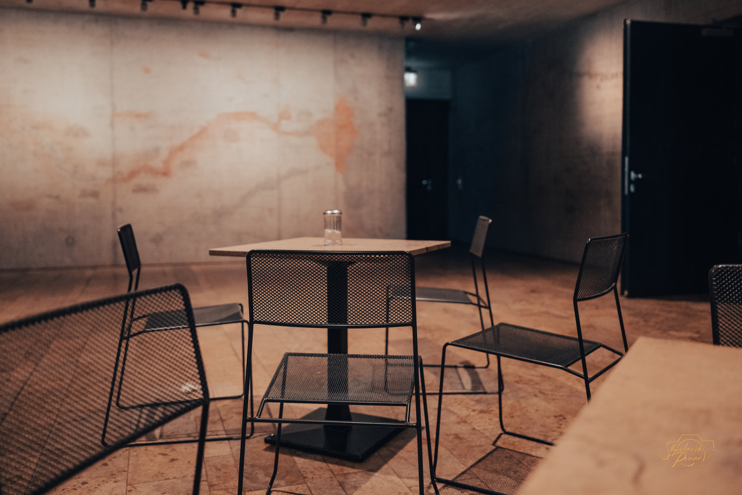 Black mesh chairs around a table in a dim concrete interior