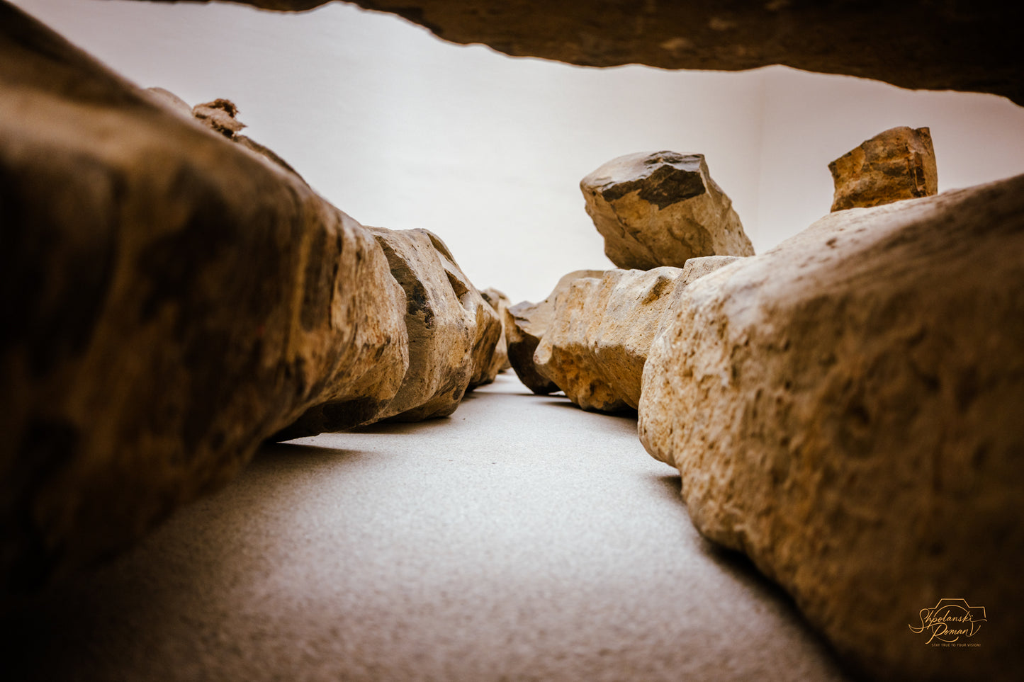 Boulders over a softly lit passage in a cave-like interior, second view