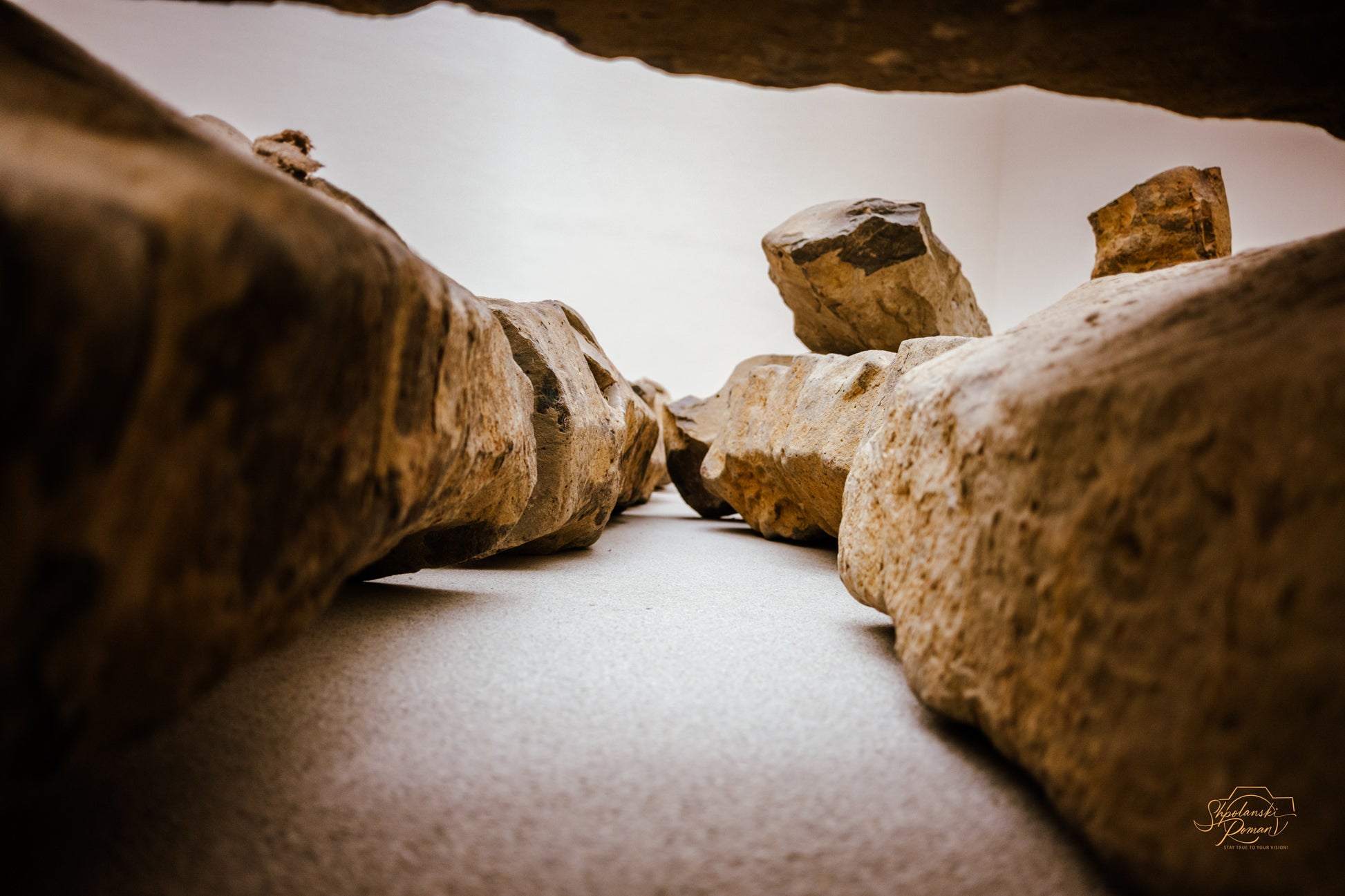 Boulders over a softly lit passage in a cave-like interior, second view