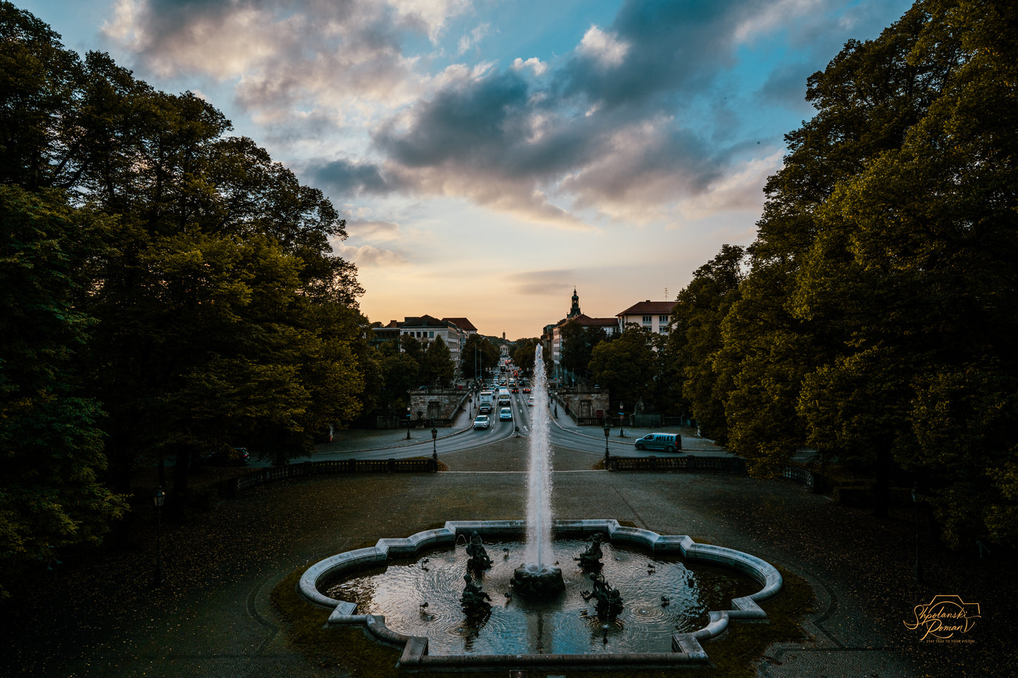 A fountain on a tree-lined avenue at twilight in Munich